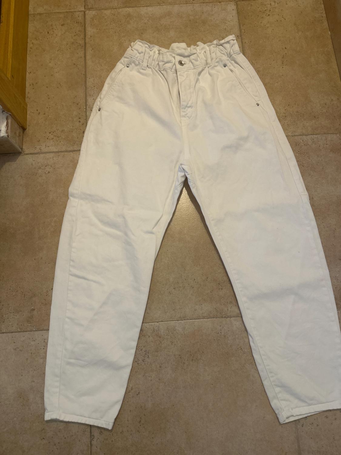 White, button-front, shirred-waist trousers, laid on a beige tiled floor.