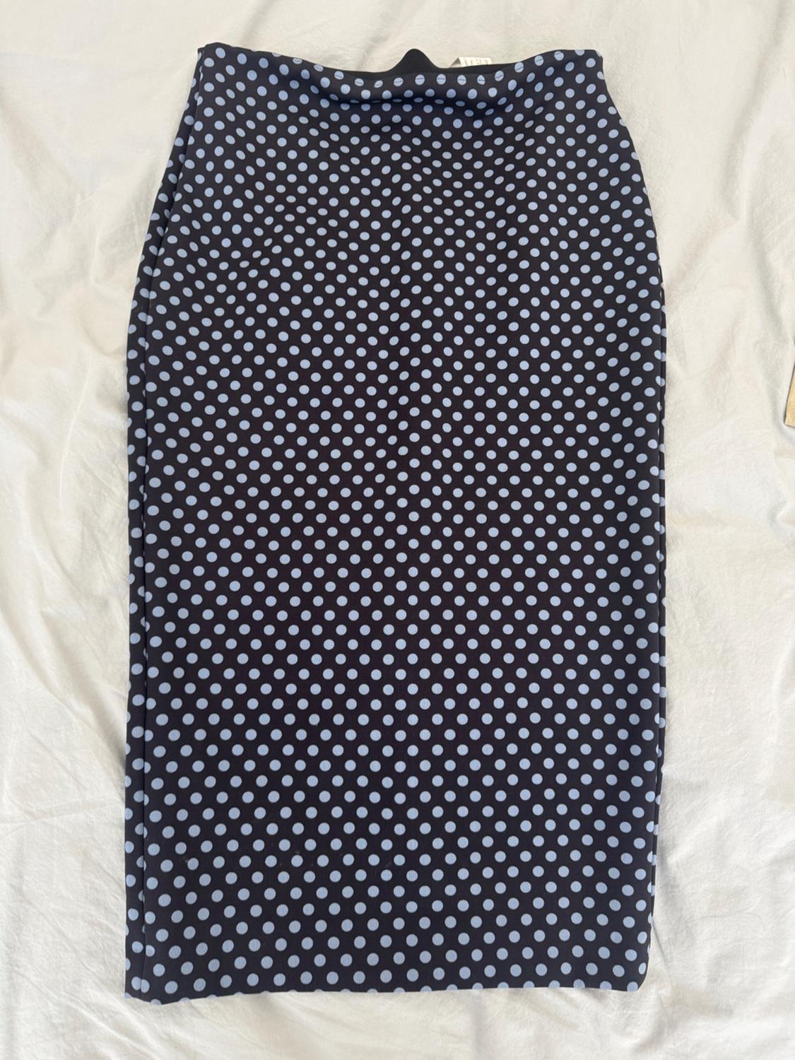 Dark midi skirt with a light polka-dot pattern, laid out on a background of crumpled white fabric.