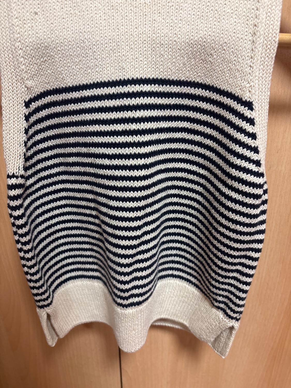 Cream-coloured knitwear with dark horizontal stripes in the centre and slits at the hem, on a wooden background.