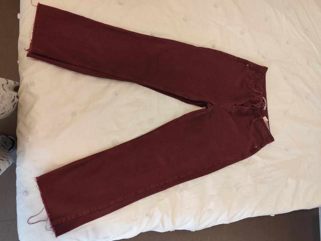 Burgundy denim jeans with a frayed hem, placed on a white quilt with button details.