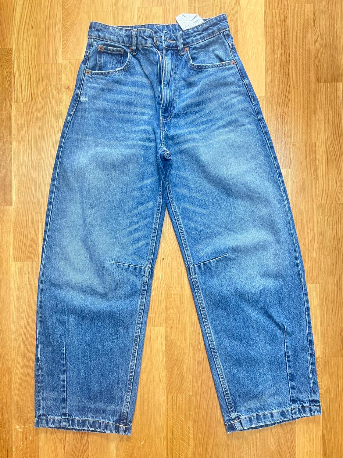 Blue straight-leg jeans on a light wooden floor. Visible front pockets and waist label.