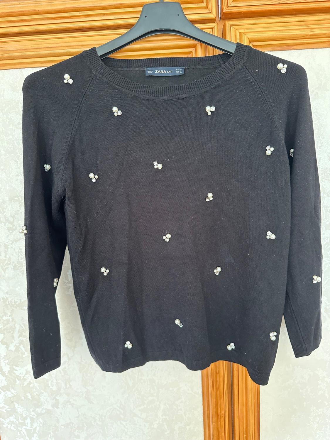 Front view of black jumper with small pearl appliqués, crew neck and long sleeves.