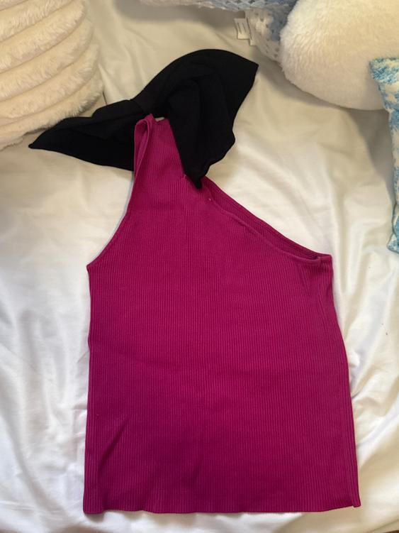 Fuchsia asymmetrical top with a black bow on a white bed, surrounded by white and blue cushions.