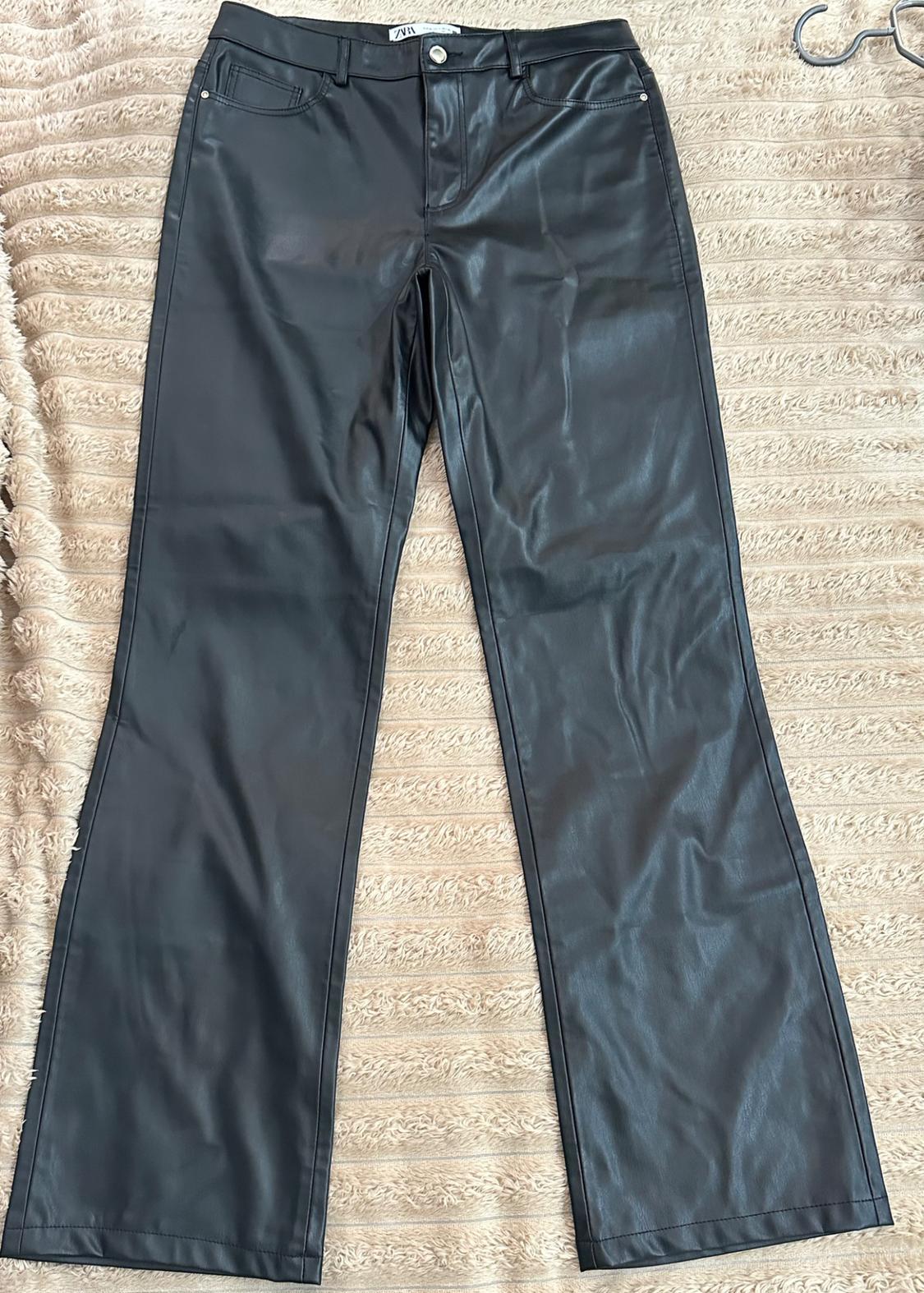 Black straight-cut trousers on a textured beige rug. Button and pockets visible. "Zara" label at the waist.