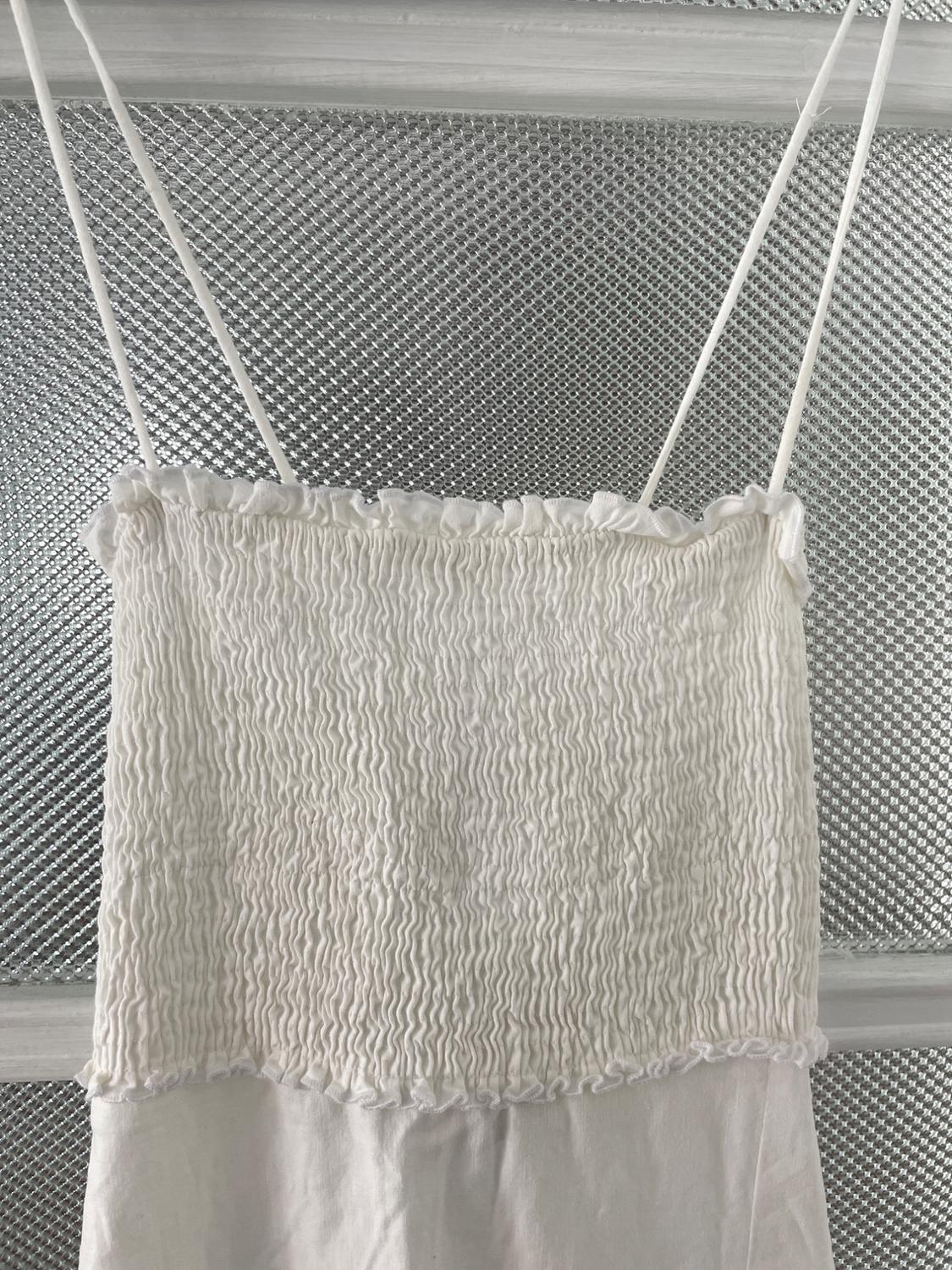 White dress with thin straps and ruched top, hung in front of a textured metallic background.