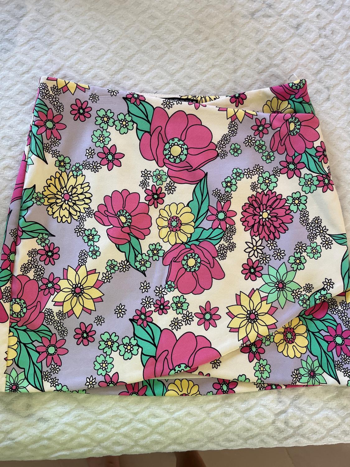 Short skirt with a pink, yellow, and green floral print on a lilac and white background, laid on a white textured surface.