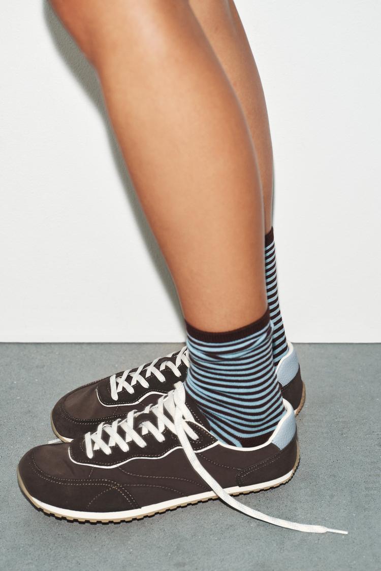 Plano medio de zapatillas marrones con cordones blancos y detalle azul en el talón, combinadas con calcetines de rayas azules y negras.
