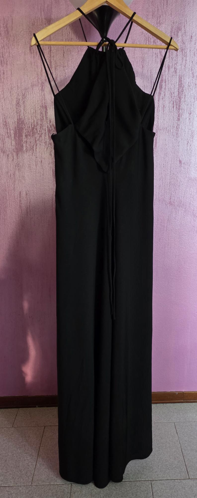 Long black dress with thin straps, hanging on a wooden hanger. Textured pink wall background.