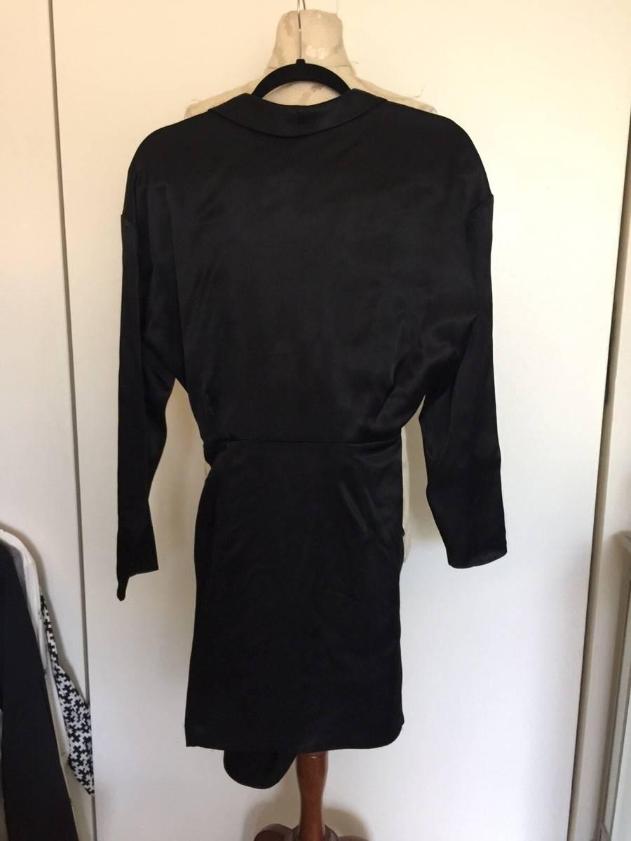 Long-sleeved black dress on a mannequin, viewed from behind. White background with clothes hanging on the left.