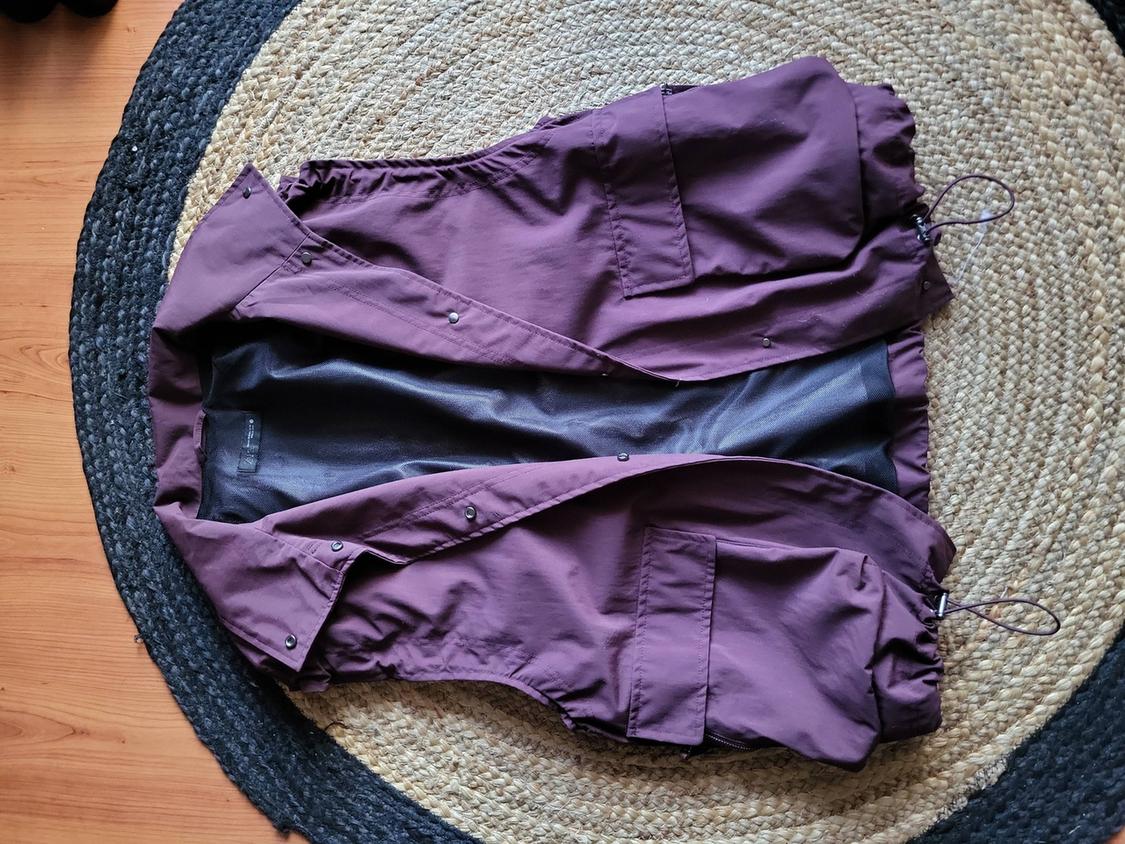Purple sleeveless waistcoat with large pockets, on a round jute rug on a light wooden floor.