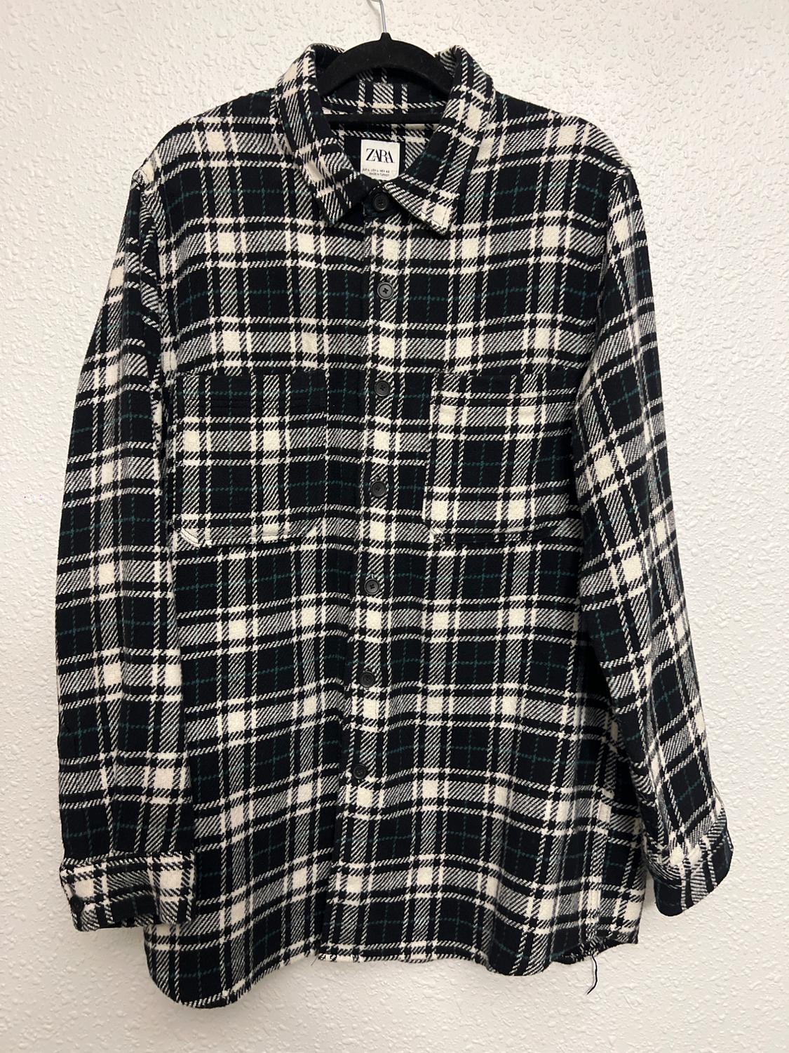 Black and white checked shirt hanging on a hanger. Visible label with the text "ZARA". White wall background.
