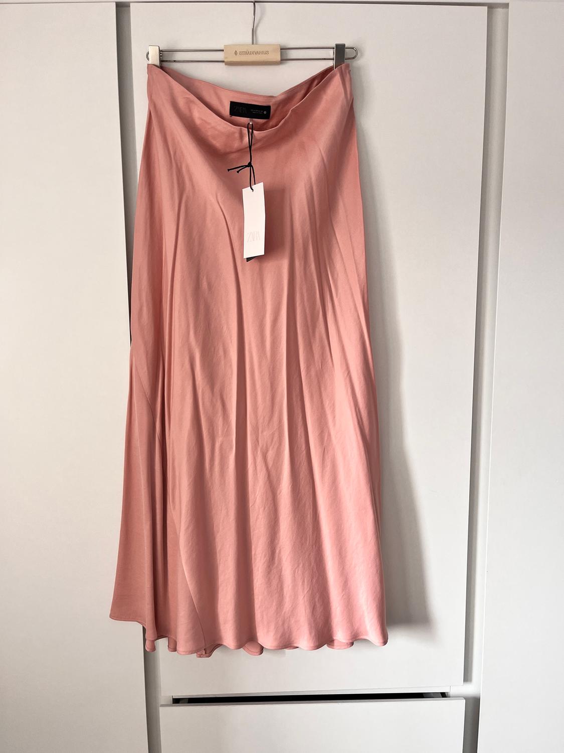 Pink skirt hanging on a wooden hanger with a visible Zara tag, against a white background.