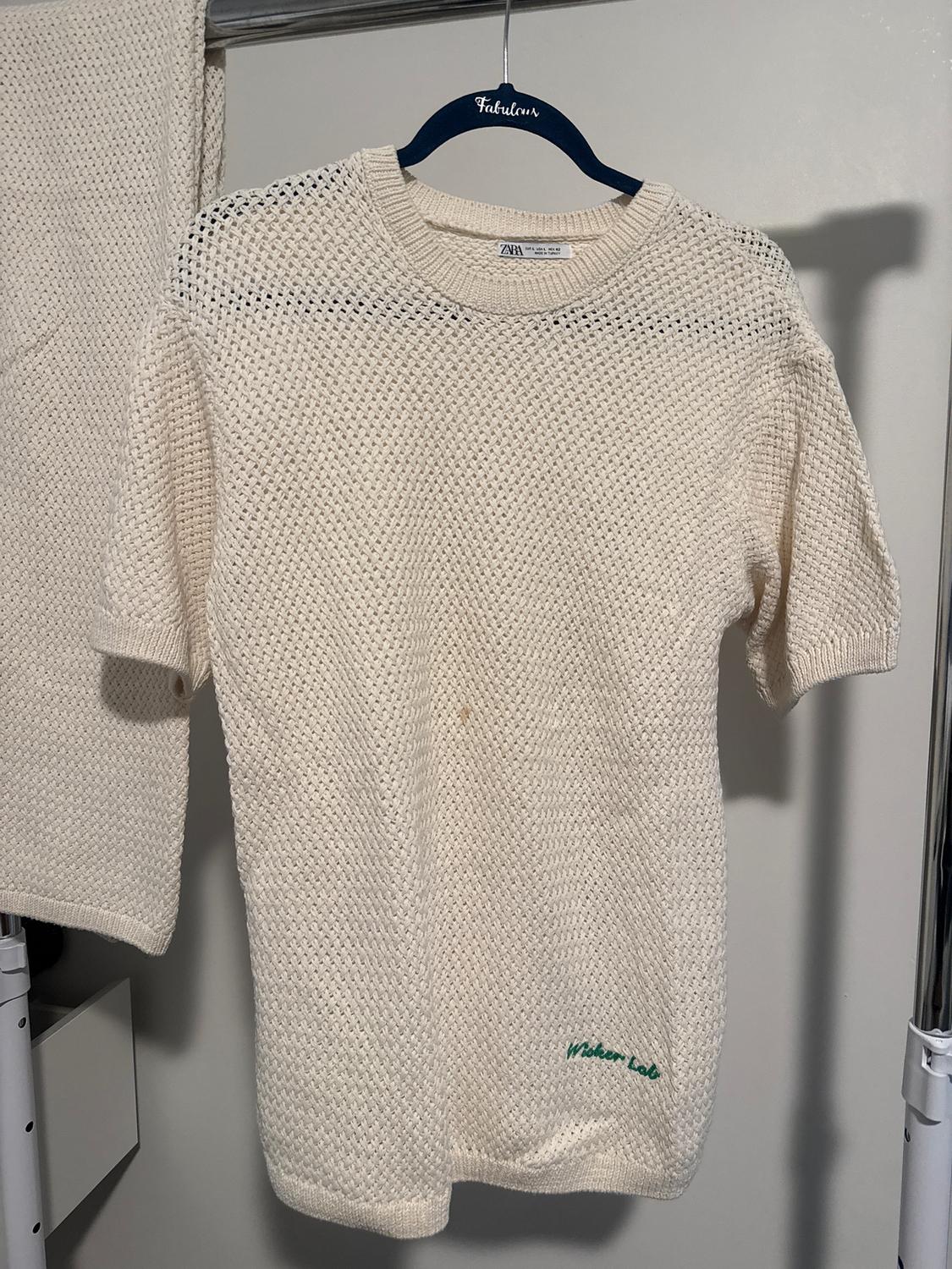 Cream-coloured knitted T-shirt hanging on a blue hanger with the word "Fabulous". "Wicker Lab" text in green at the bottom.
