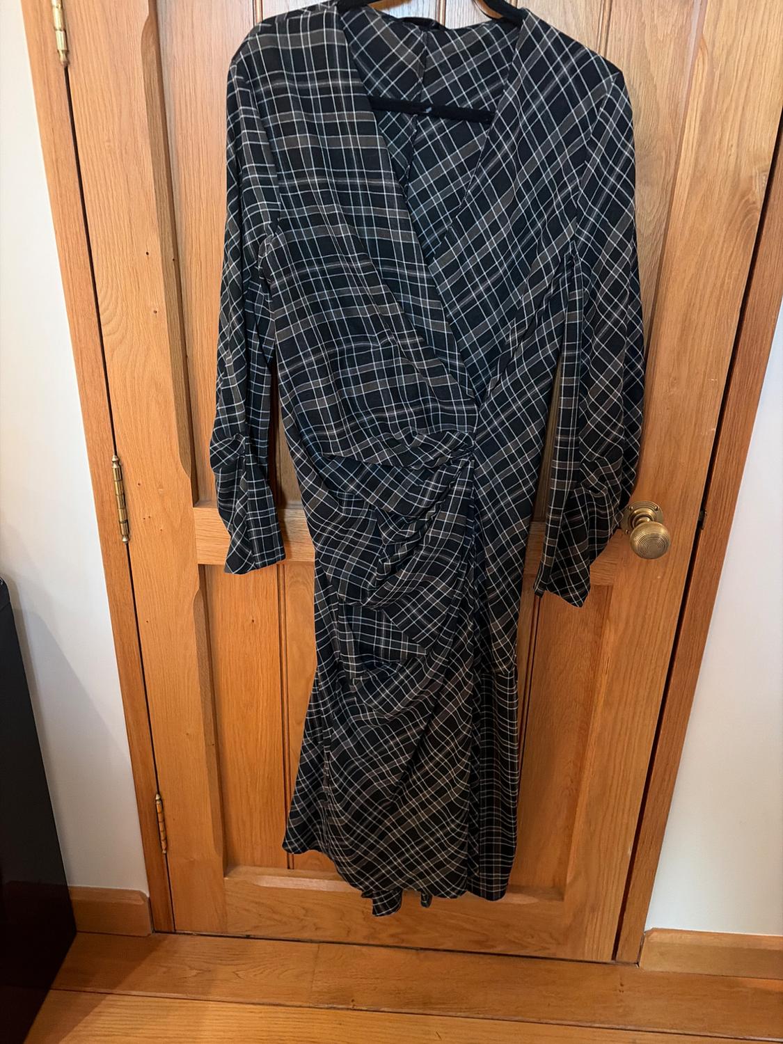 Black and white checked dress hanging on a wooden door. Wrap design with ruched waist and long sleeves.