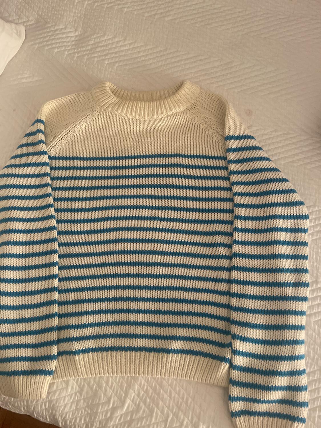 Blue and white horizontal striped jumper on a white bed. The jumper has a round neck and long sleeves.