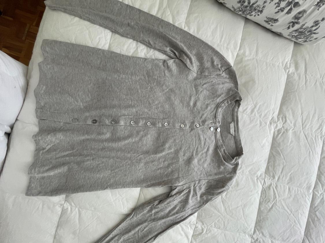 Grey long-sleeved button-up shirt, laid out on a white quilted duvet next to a floral pillow.