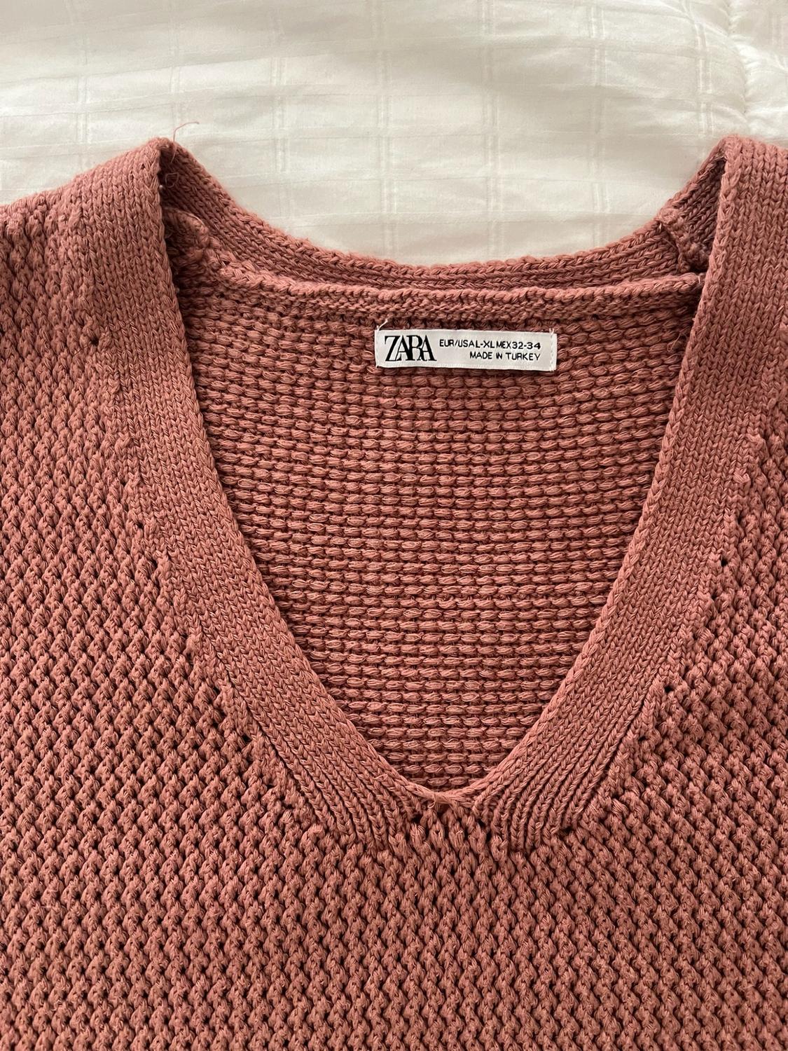 Close-up of a pink knit sweater with a V-neck. Text on label: ZARA EUR/USA L-XL MEX 42-44 MADE IN TURKEY.