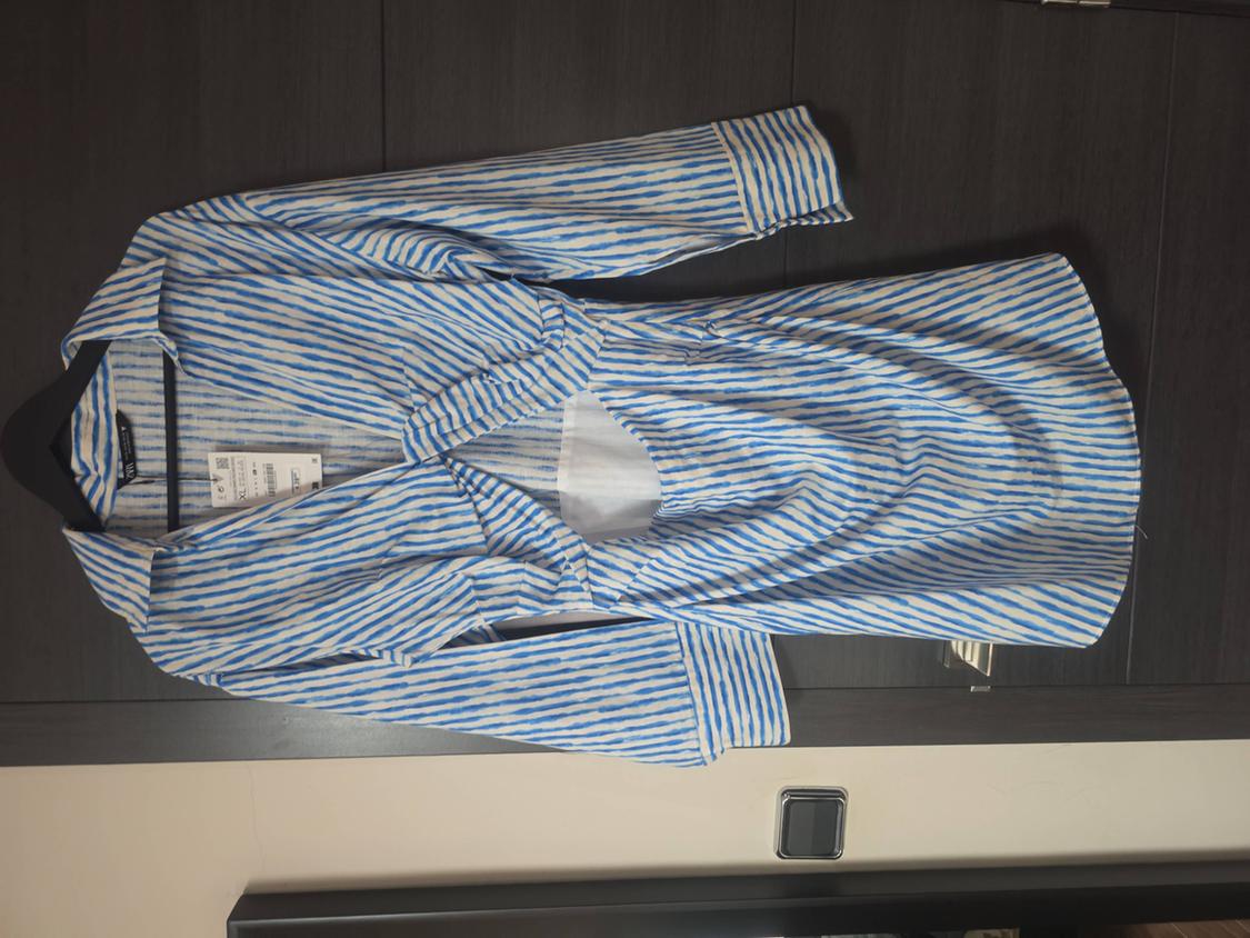 Blue and white striped long-sleeved dress with a front opening, hanging on a black hanger over a dark wooden door.