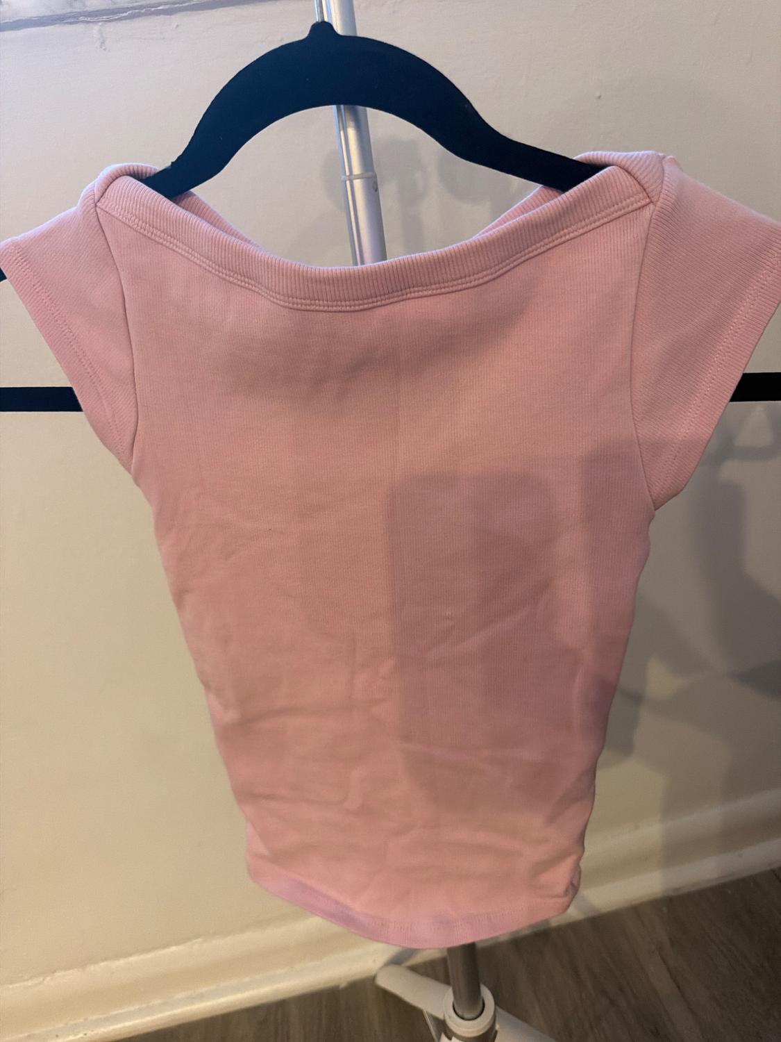 Casual light pink short-sleeved ribbed t-shirt, hanging on a black hanger on a metal clothing rack in front of a white wall.
