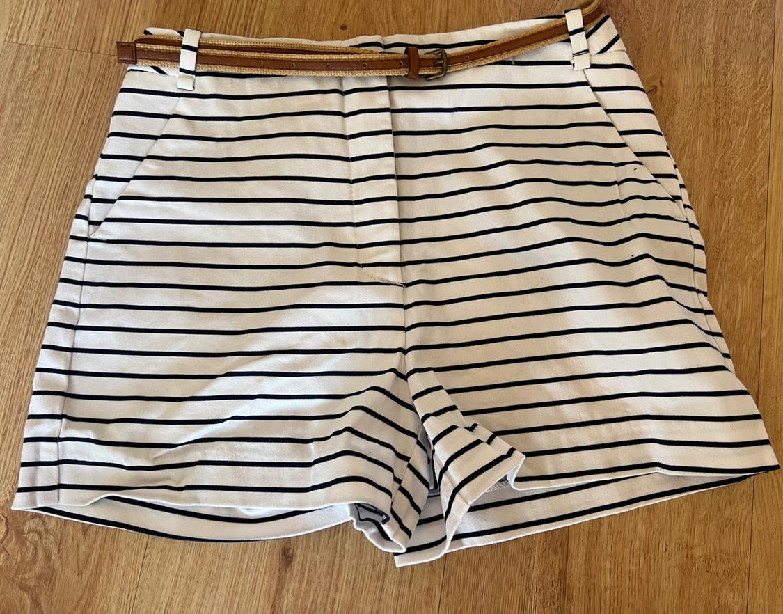 White shorts with black horizontal stripes and a braided brown belt, on a wooden floor. Casual and relaxed style.
