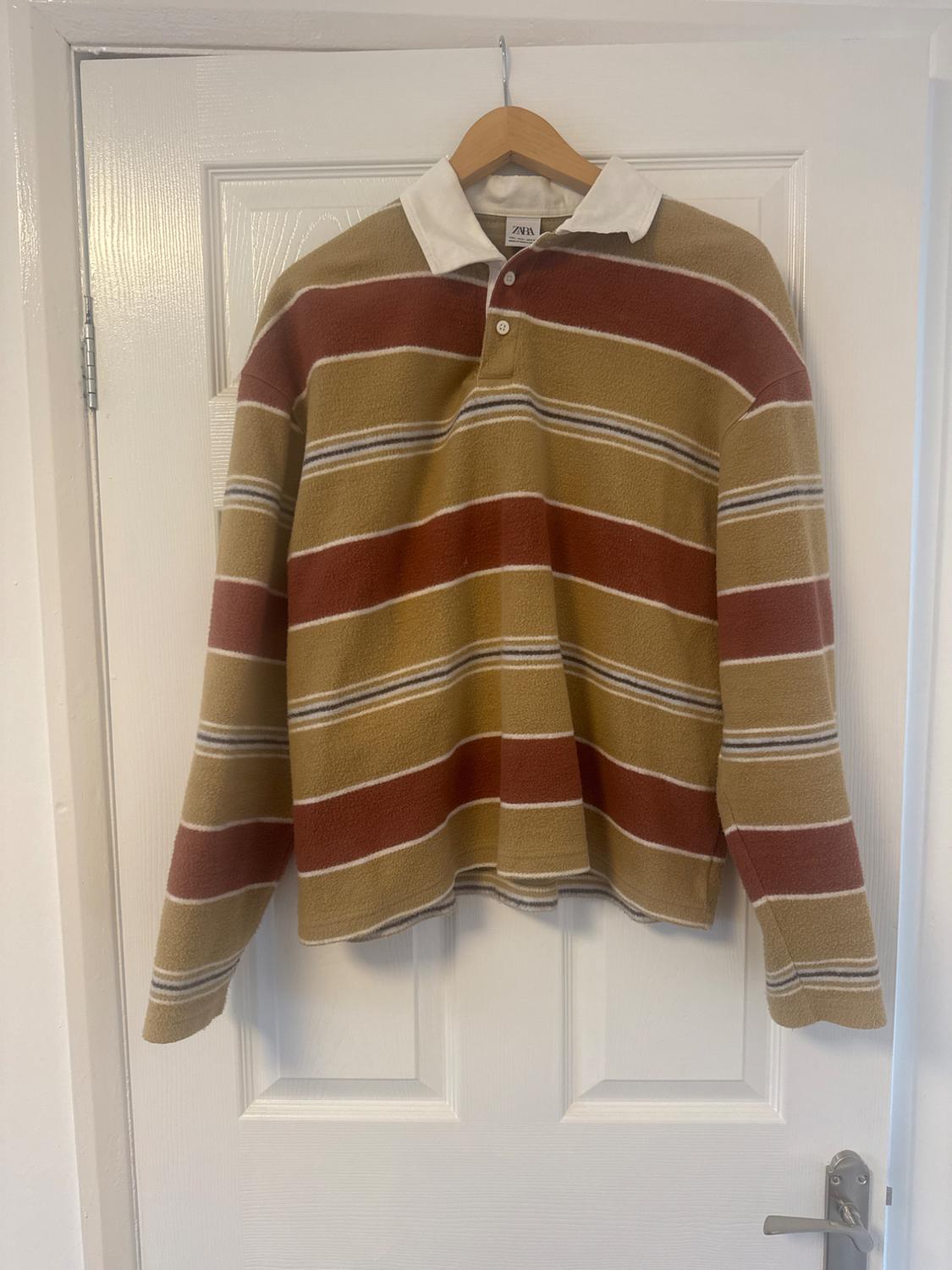 Horizontal striped jumper in brown and beige tones with a white collar, hanging on a hanger over a white door.