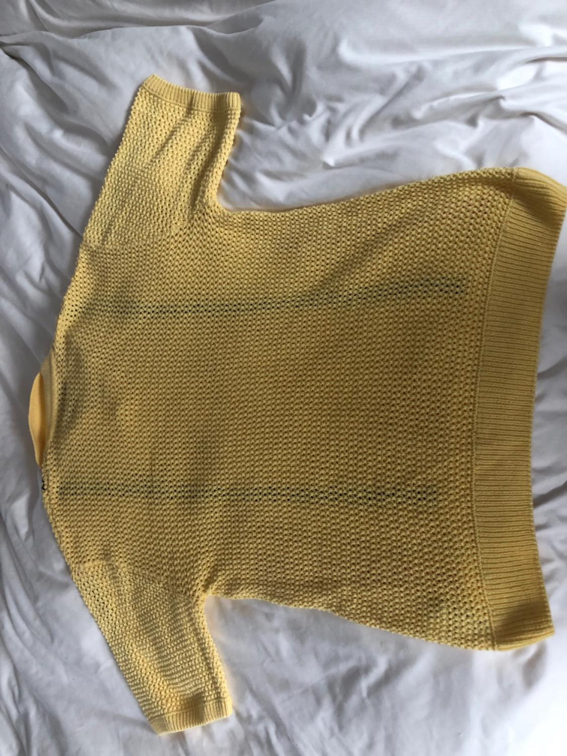 Yellow chunky knit jumper laid out on a bed with crumpled white sheets.