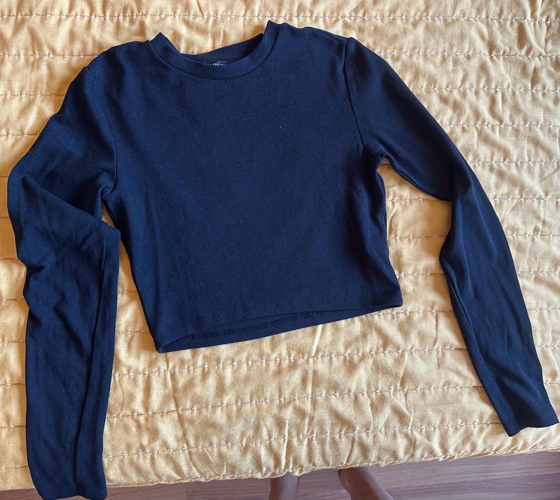 Black long-sleeved crop top with a round neck laid out on a yellow quilted bedspread.