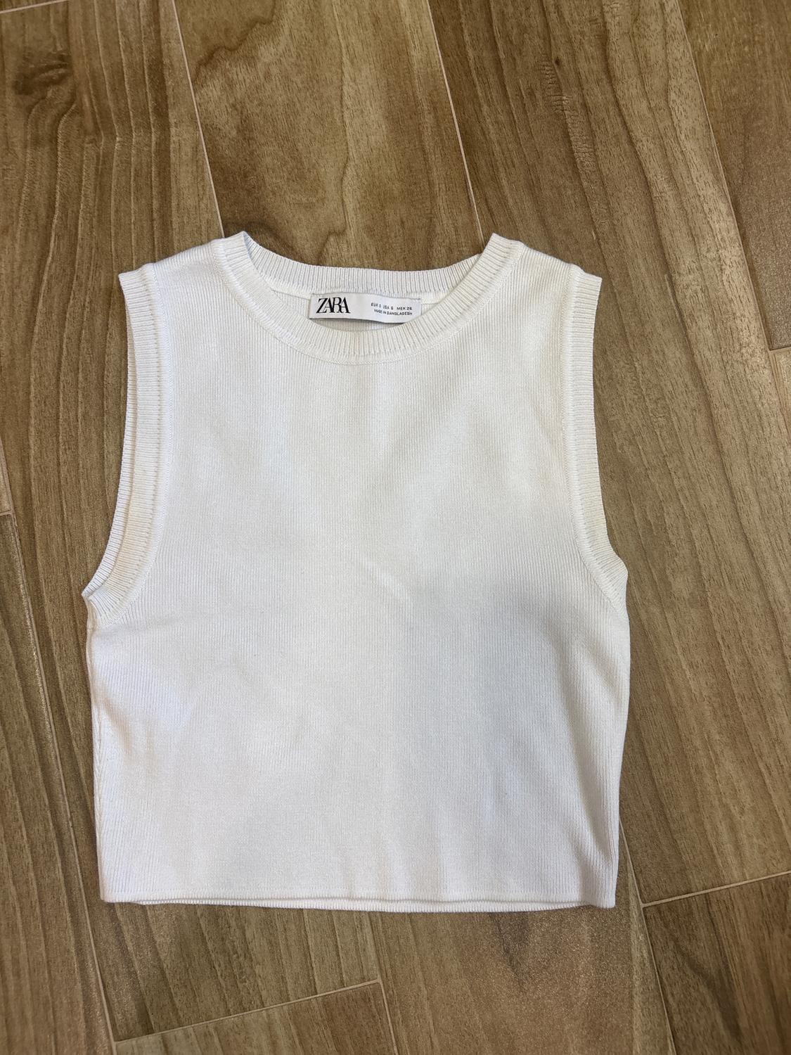 White knitted tank top on a wooden floor. Visible label with text: "ZARA".