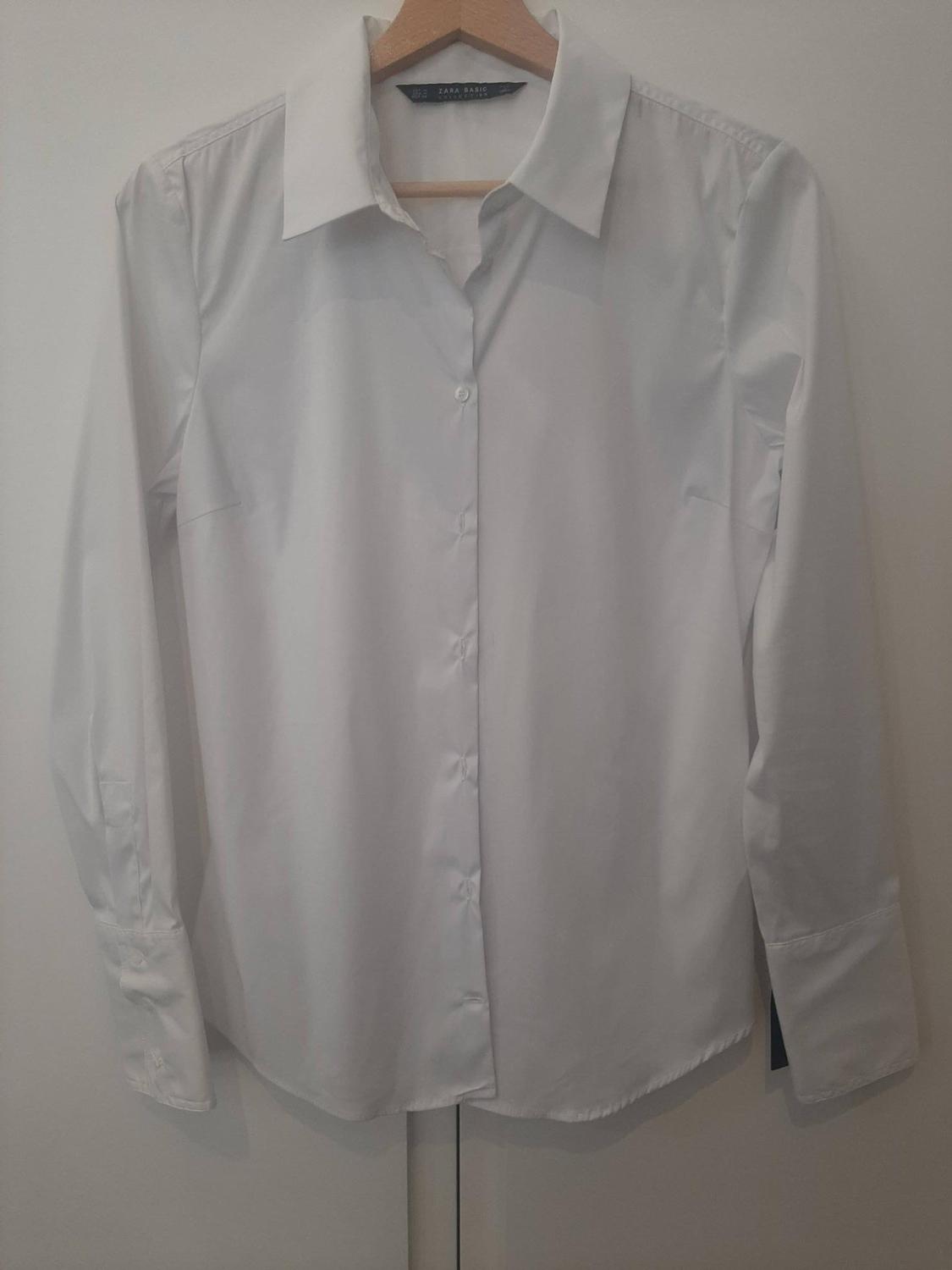 White long-sleeved shirt hanging on a wooden hanger. Visible label: "ZARA BASIC". White background.
