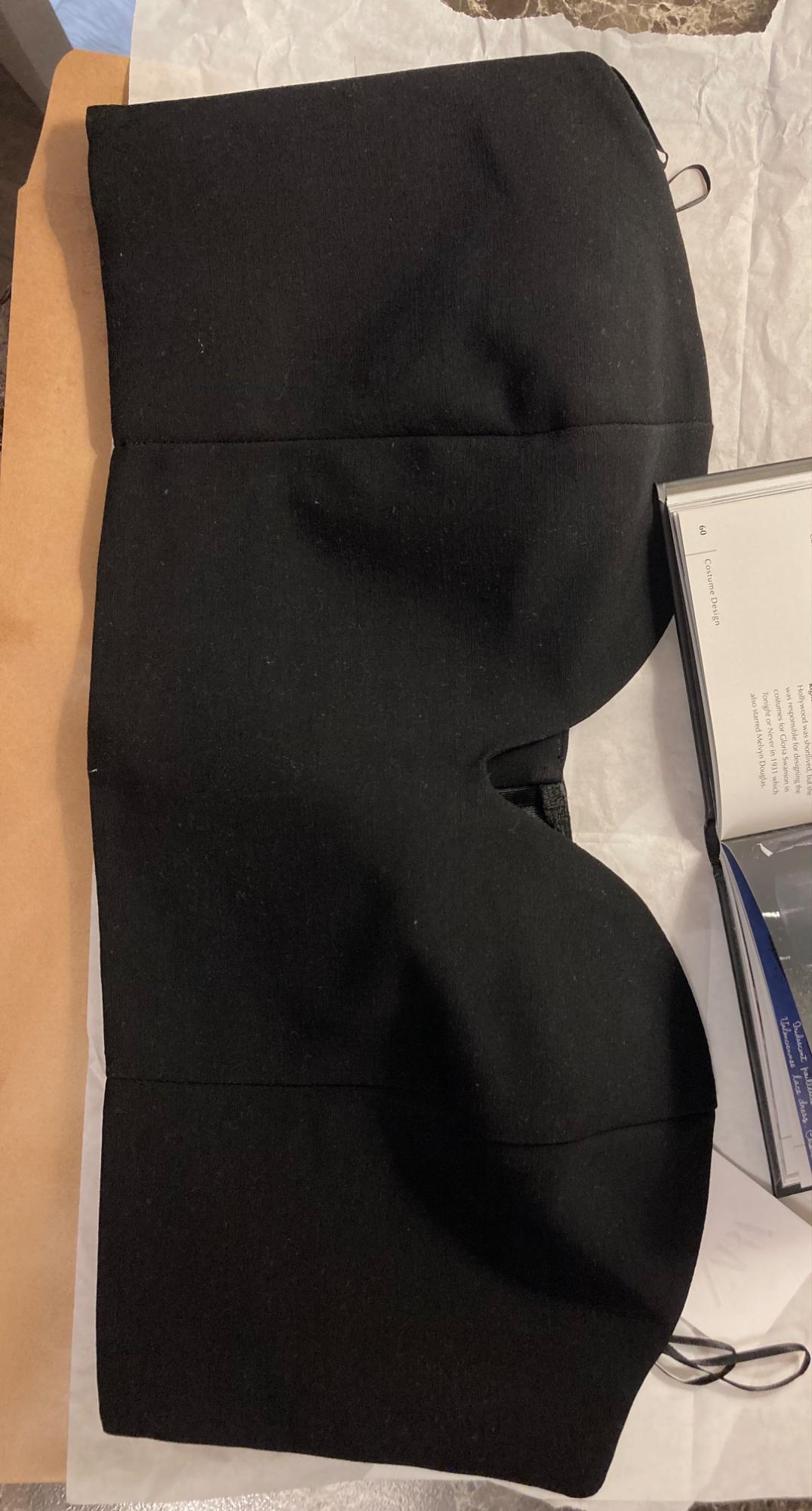 Black strapless top on white paper, next to an open book with visible text. Brown cardboard background.