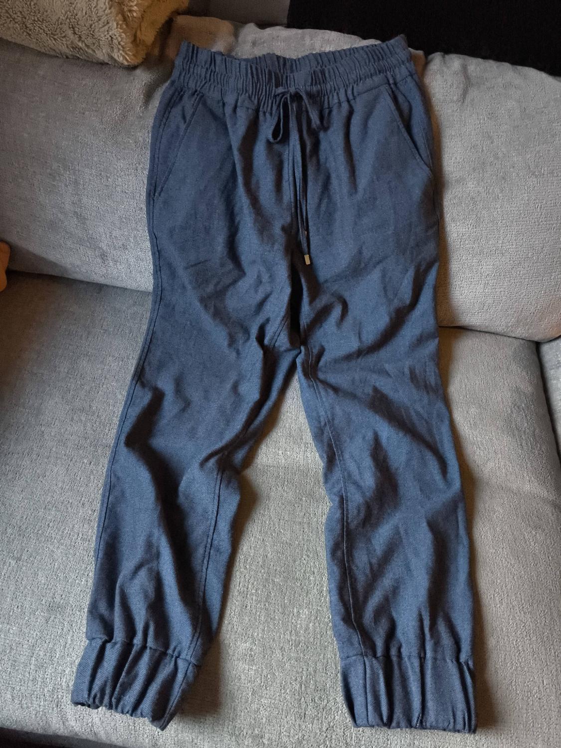 Dark blue tracksuit bottoms with an elasticated drawstring waist, placed on a light grey sofa.