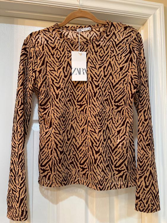 Long-sleeved sweater with animal print in brown and black tones, hanging on a wooden hanger. Visible label with "ZARA" text.