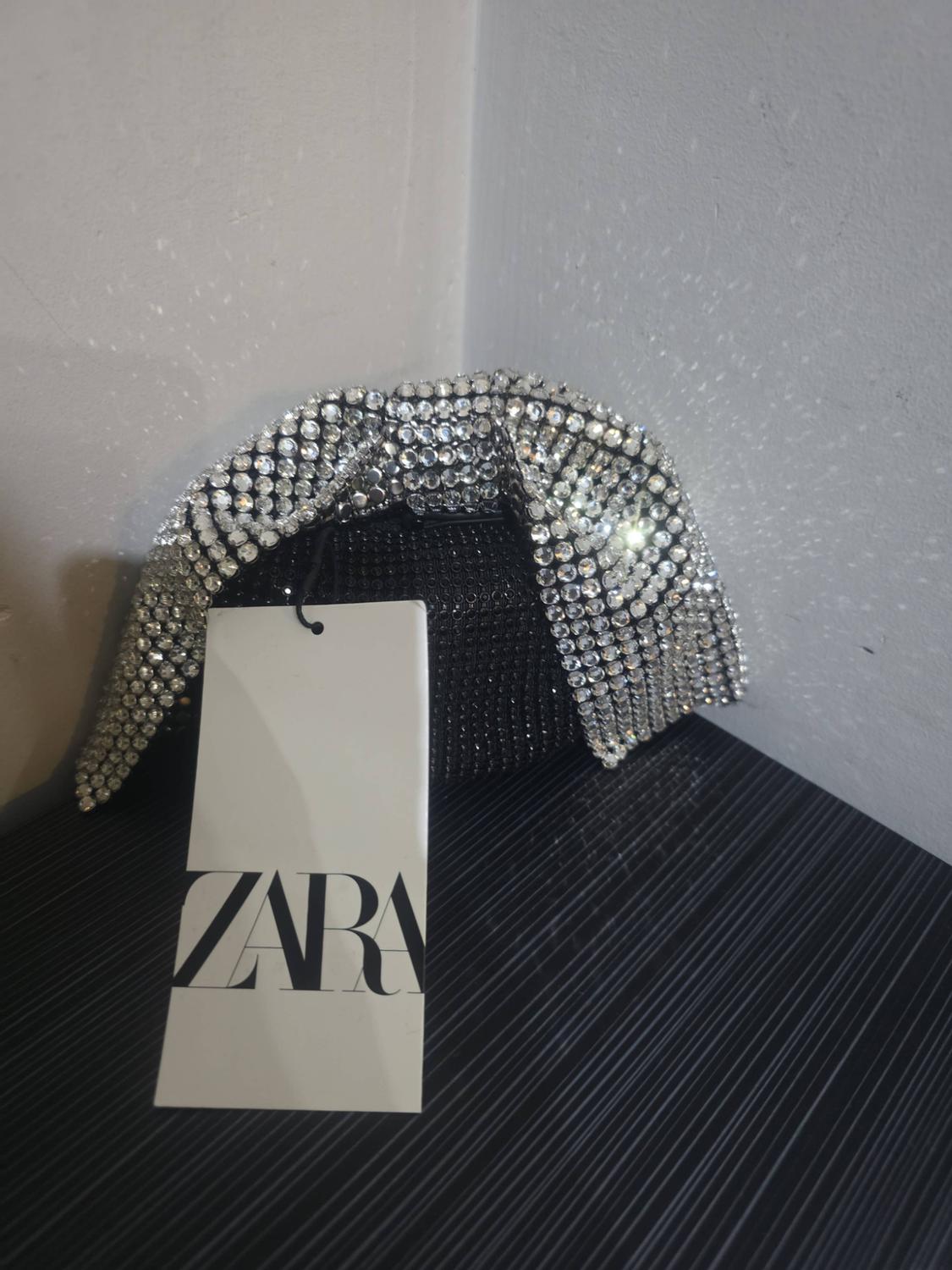 Black handbag with rhinestones and a knotted handle featuring shiny silver crystals. A white tag hangs from it with the text ZARA.