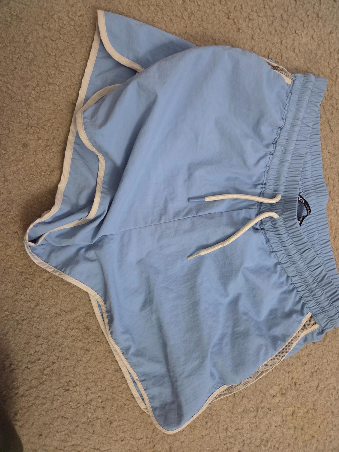 Blue shorts with white trim and drawstring, placed on a beige rug.