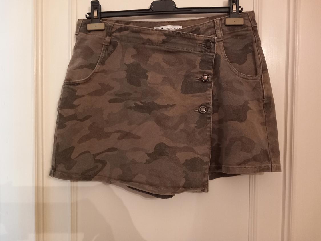Short camouflage wrap skirt with three metallic buttons. Hanging on a black hanger over a white door.
