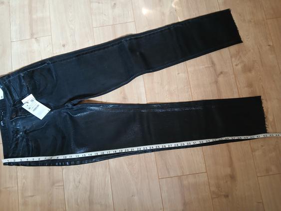 Black leather trousers on a wooden floor with a tape measure along the leg. Visible label on the waistband.