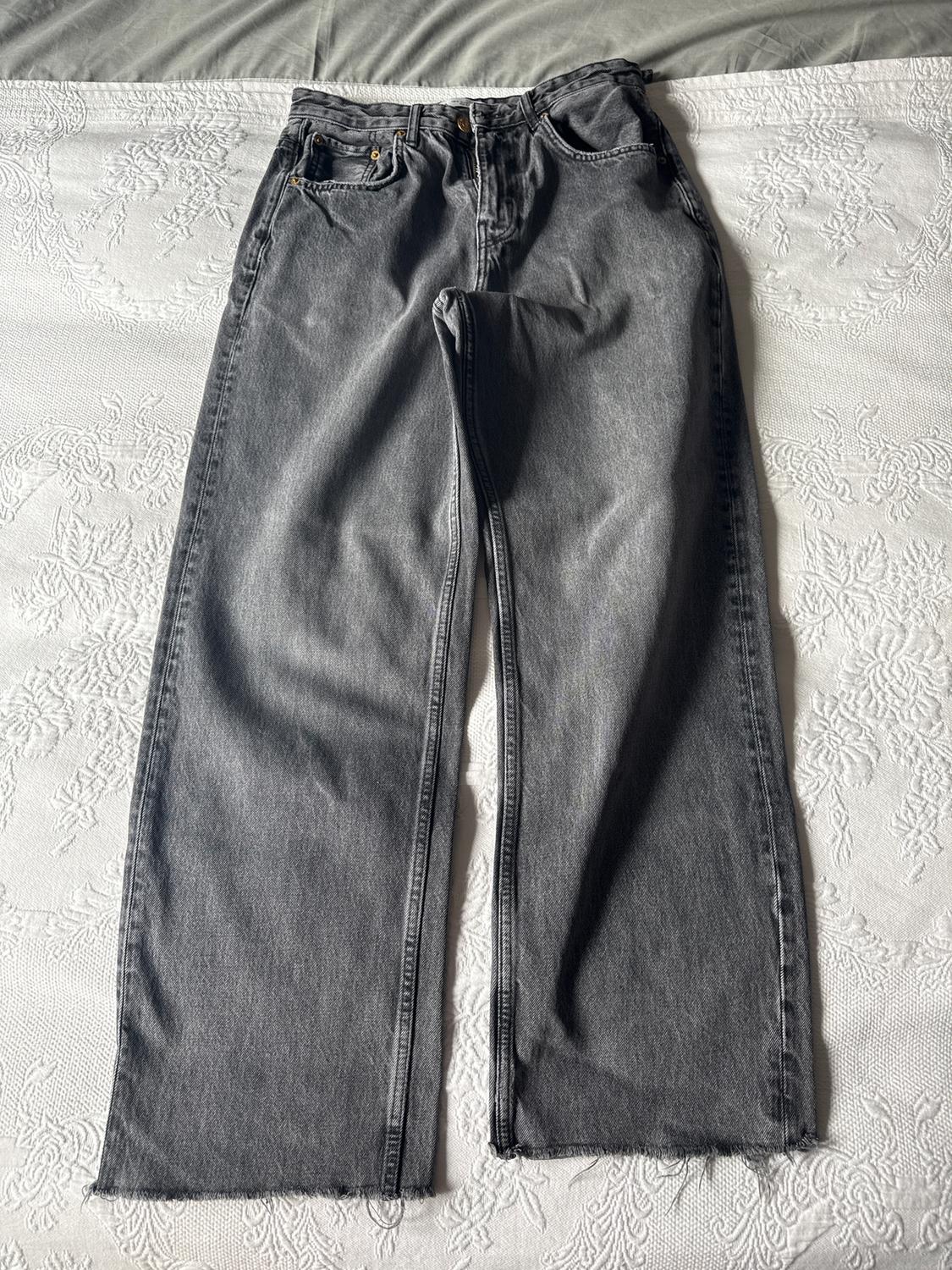 Grey wide-leg jeans with a frayed hem, placed on a white floral-patterned bedspread.