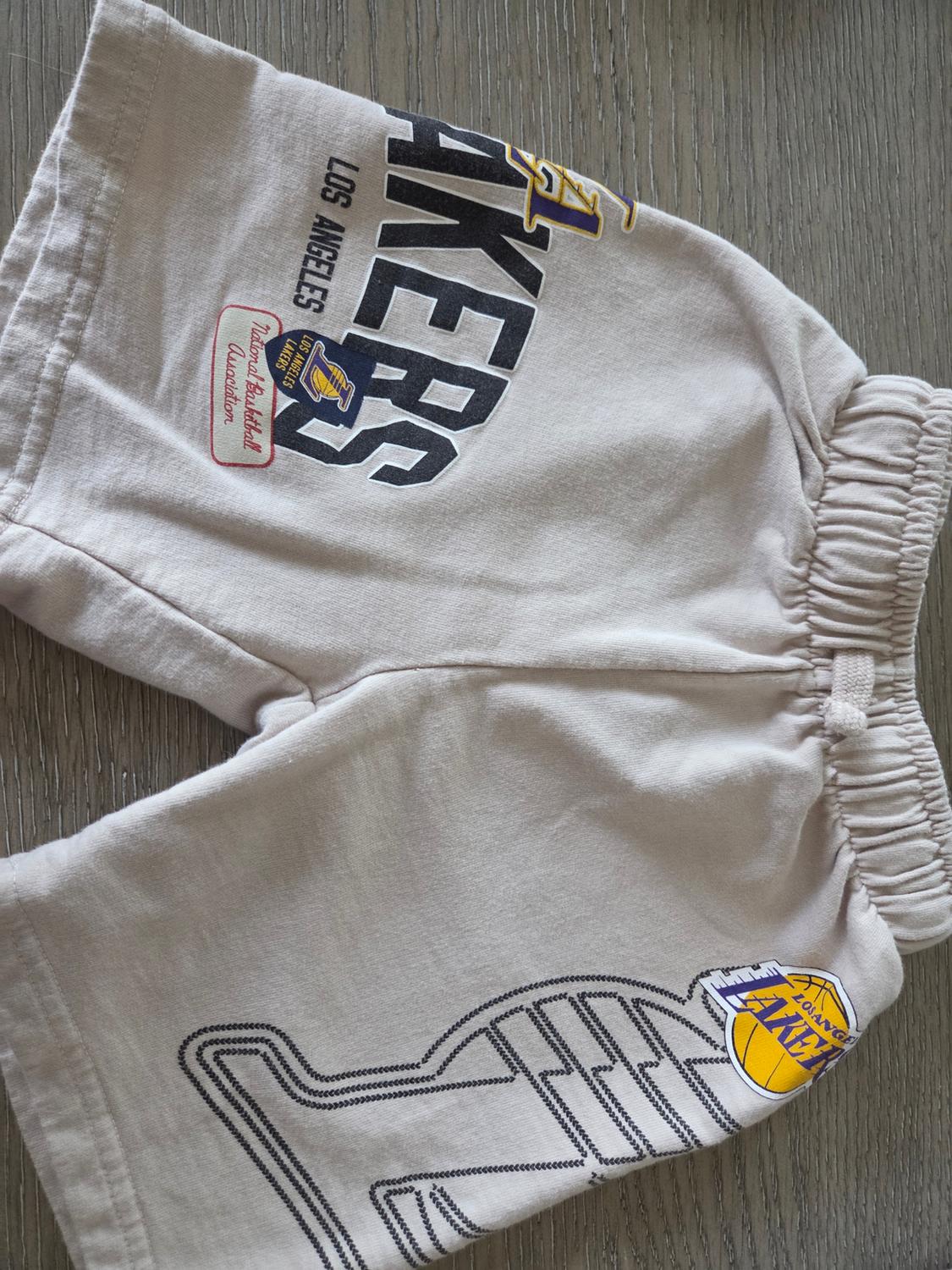 Beige shorts with the Los Angeles Lakers logo and "National Basketball Association" text on a wooden surface.