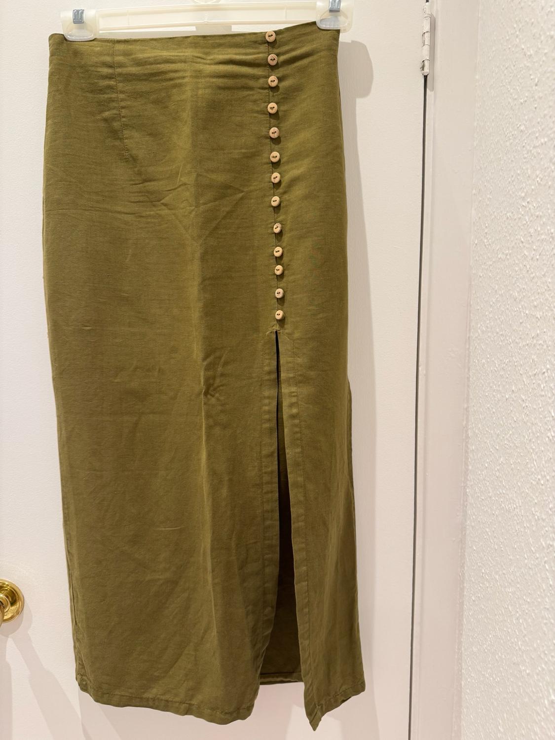 Olive green long skirt hanging on a white door. It has a row of buttons on one side and a split at the hem.