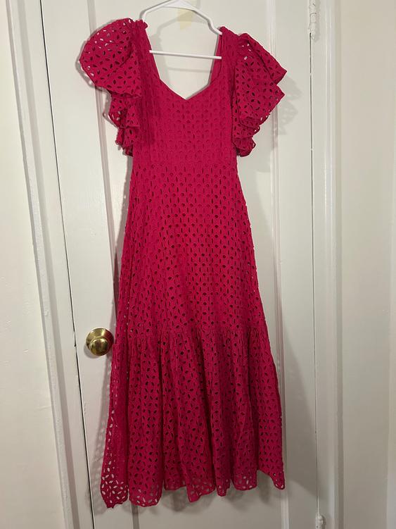 Pink dress with an openwork design, short ruffled sleeves, hanging on a white hanger over a white door.
