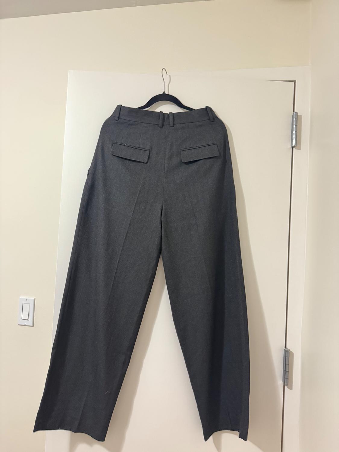 Gray wide-leg pants hanging on a black hanger over a white door. Flap back pockets.