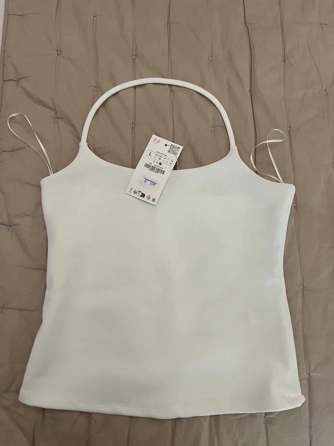 White halter-neck top with hanging ribbons, on a beige quilted background. Label with text: L, S M L, € 17.95.