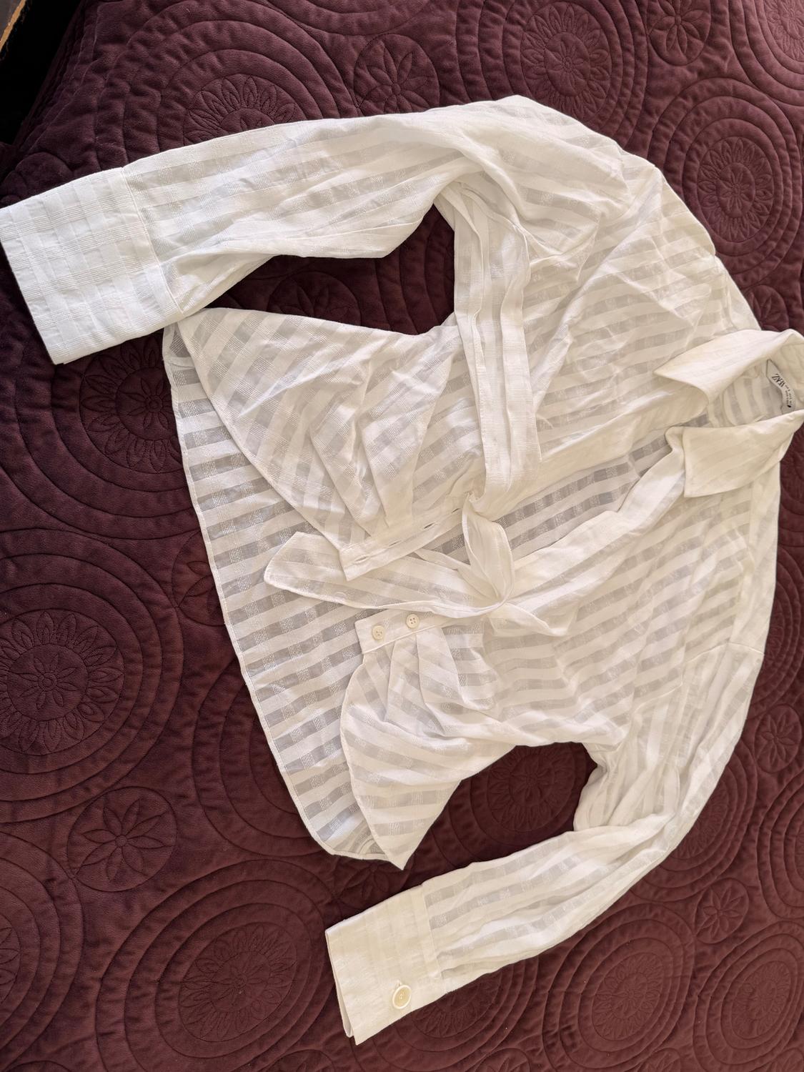 White pinstripe shirt on a purple quilted bedspread with a circular design. Long sleeves and visible buttons.