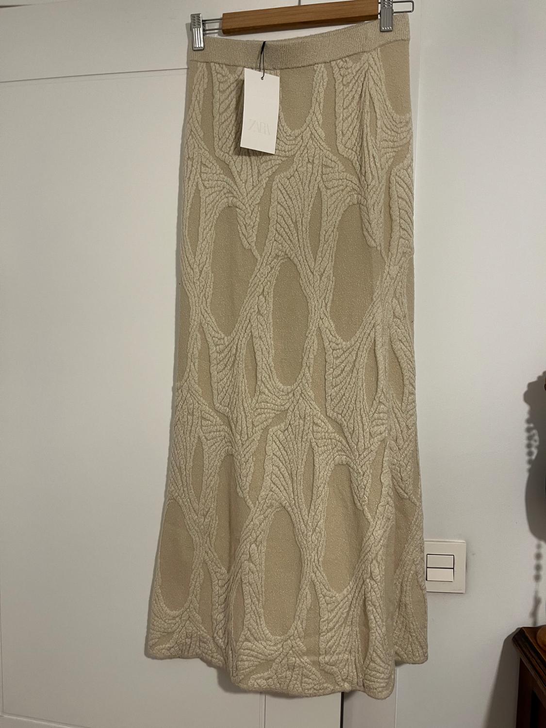 Beige skirt hanging from a hanger with a textured interwoven pattern design. Visible label with text "ZARA". White background.