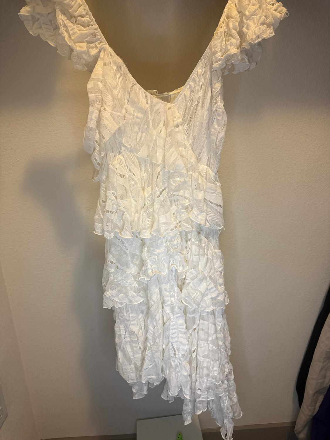 White dress with ruffles and lace hanging on a hanger against a beige wall.