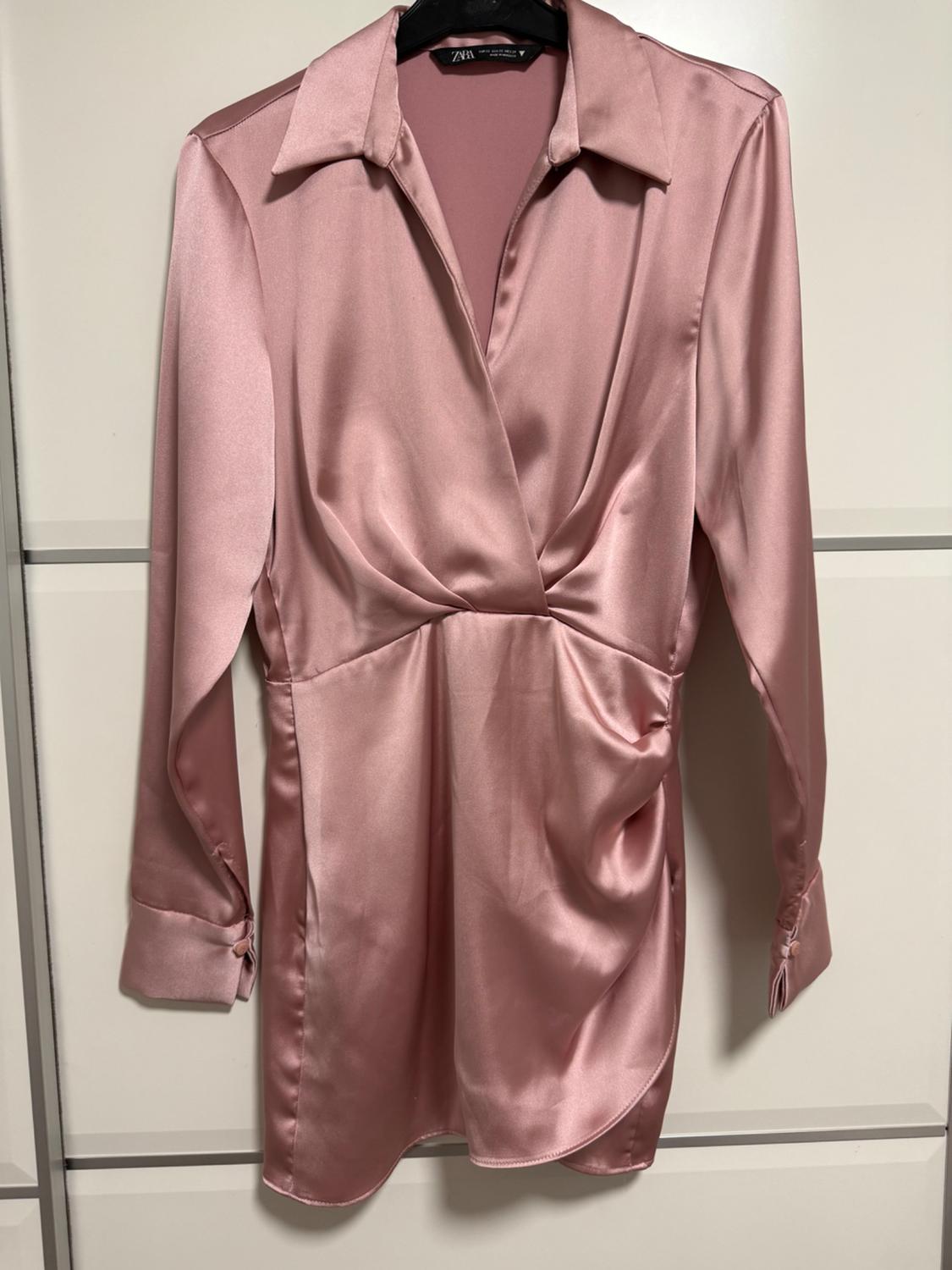 Pink satin blouse with a classic collar and long sleeves, hanging on a black hanger in front of a white background.
