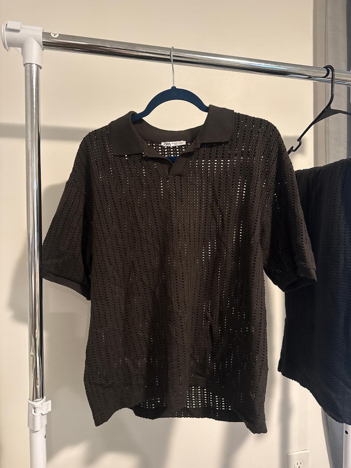 Black open-knit polo shirt hanging on a metal clothes rail. White background and light-coloured wall.