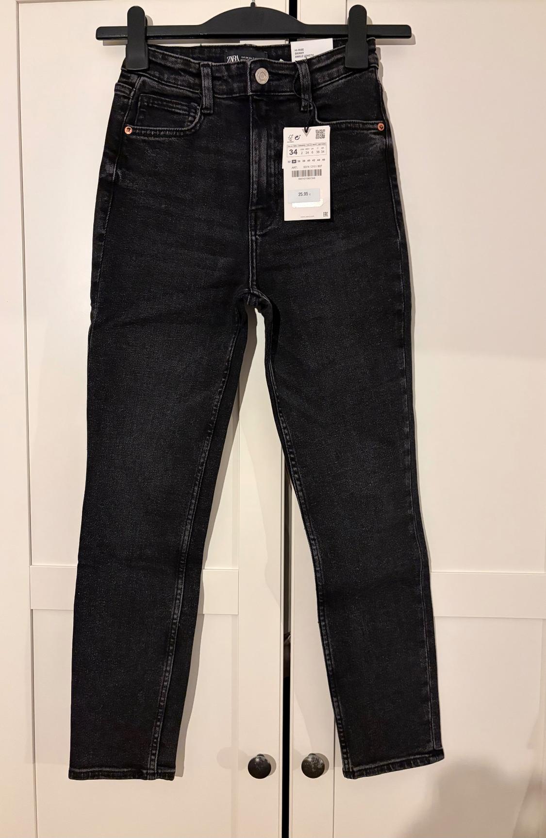 Black denim jeans hanging on a hanger with a price tag of 25.95 euros, against a white wardrobe background.
