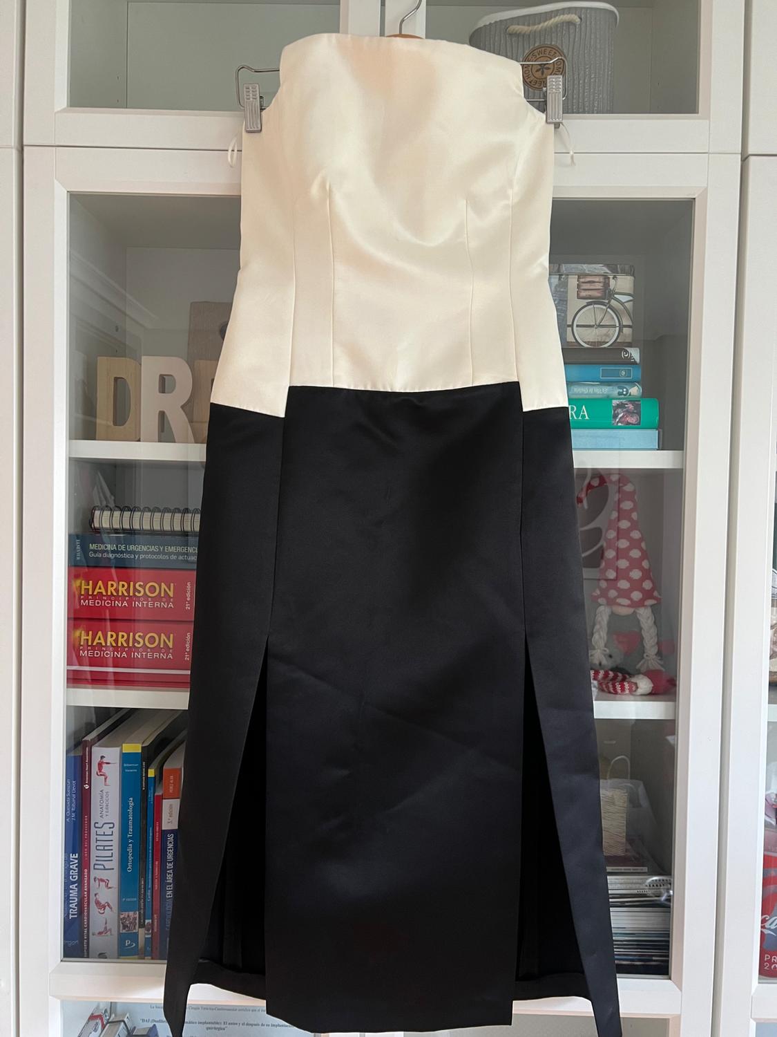 A two-tone dress hangs in a wardrobe, with a white top and a black skirt with slits. In the background, books and decorative items are visible.
