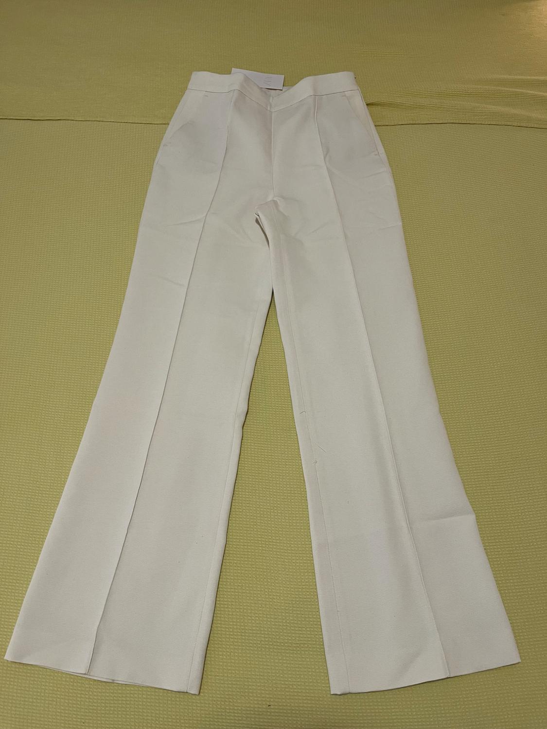 White wide-leg trousers on a yellow surface. Design with front pleats and side pockets.